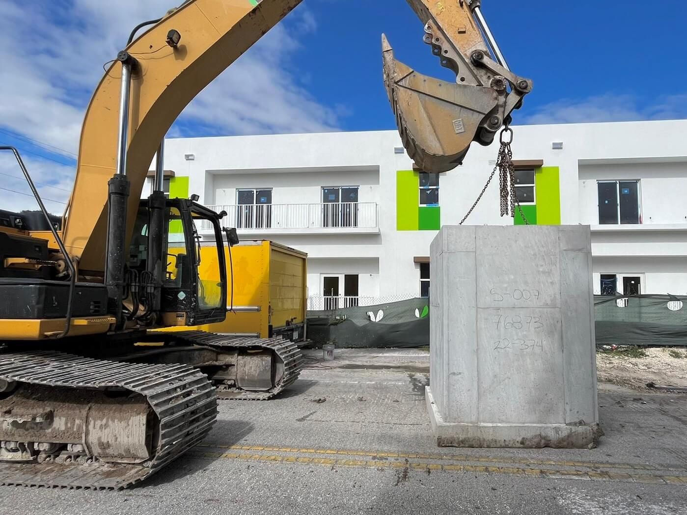 Lumix excavator setting a precast drainage structure on a Miami street